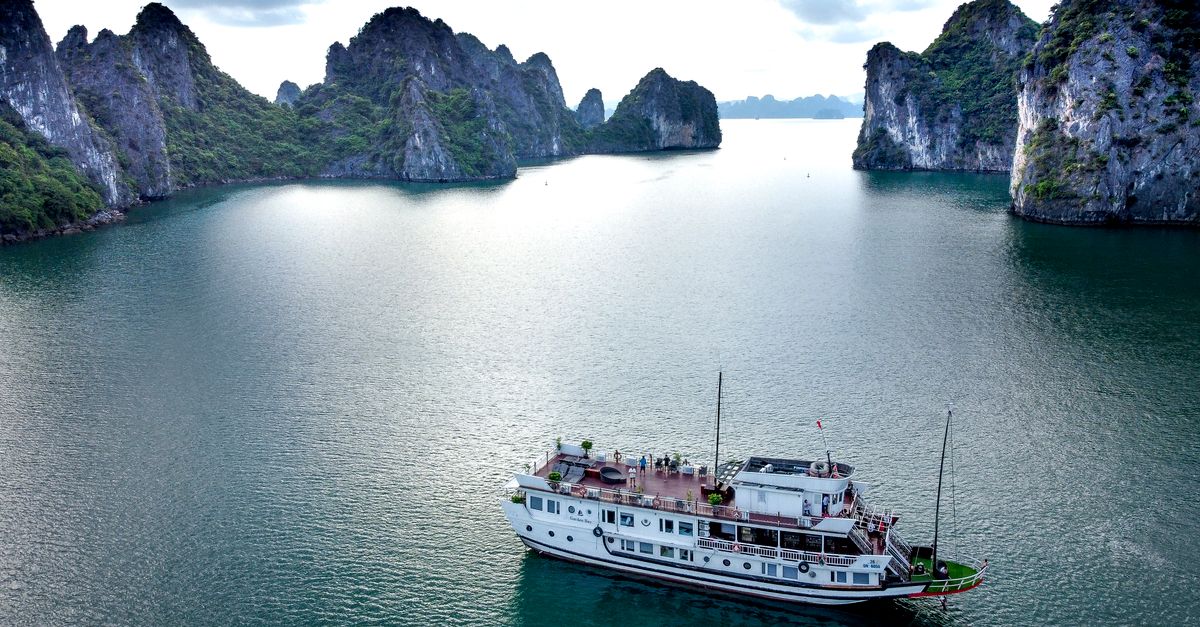 A cruise ship sails through the stunning cliffs and waters of Ha Long Bay.