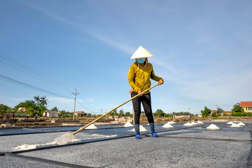Free A person using a shovel to harvest salt in outdoor salt fields under a blue sky. Stock Photo