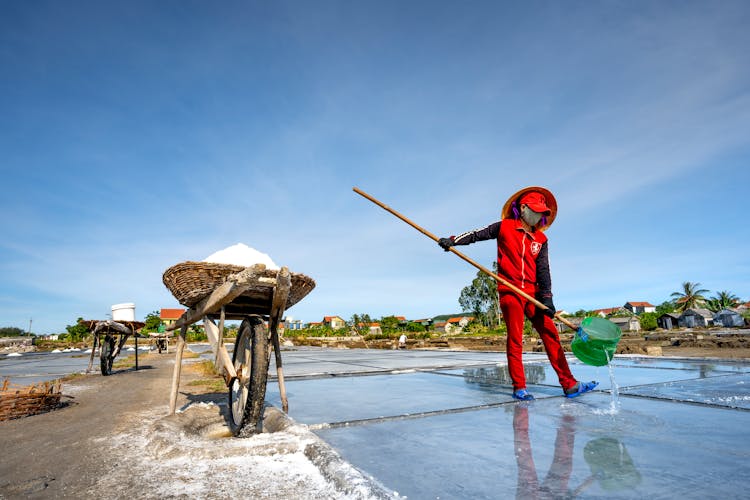 Wheelbarrow And A Man In Red Clothing Standing With A Net In Wet Field