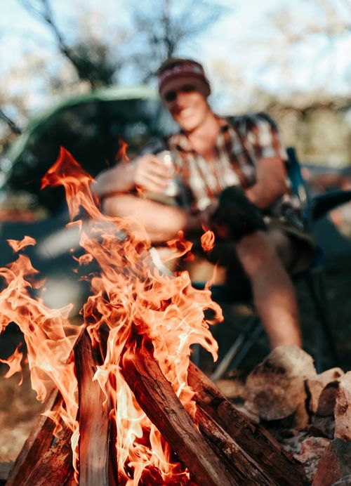 Free A man relaxes by a blazing campfire in the outdoors, enjoying the warmth and ambiance. Stock Photo