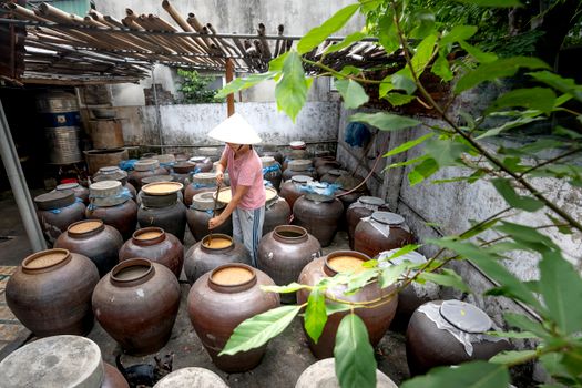 A person tends to large ceramic pots in an outdoor fermentation yard.