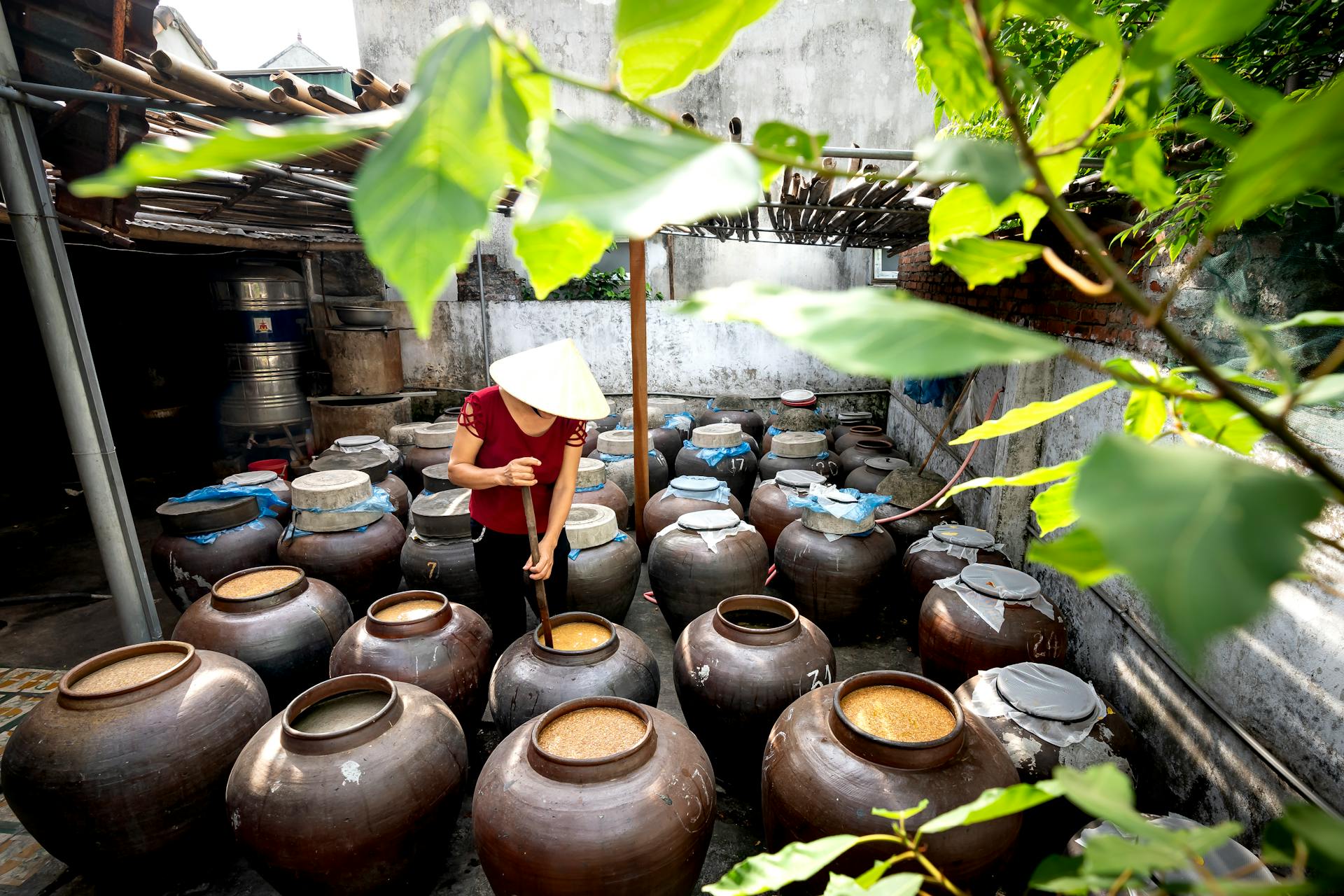 Person in Conical Hat Cooking Traditional Food in Jugs