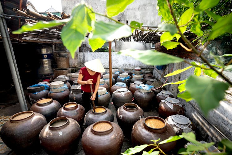 Person In Conical Hat Cooking Traditional Food In Jugs