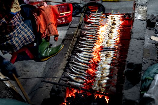 Street vendor grilling fish over open flames, showcasing traditional cooking method.