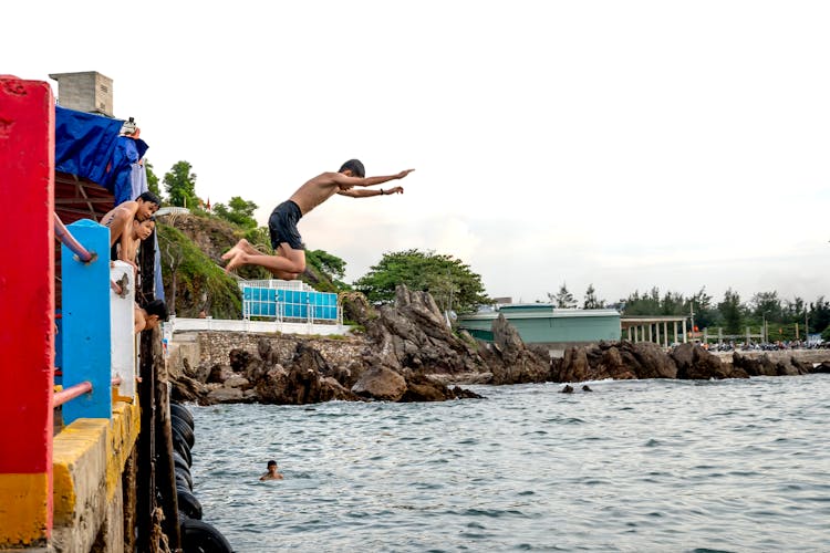 Young Man Jumping From A Pier Into The Water 