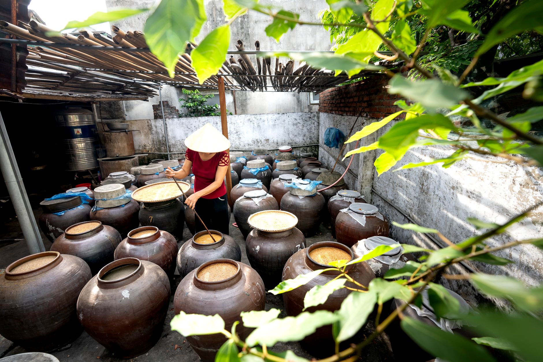 Woman wearing a hat tending to clay pots in an outdoor storage area.