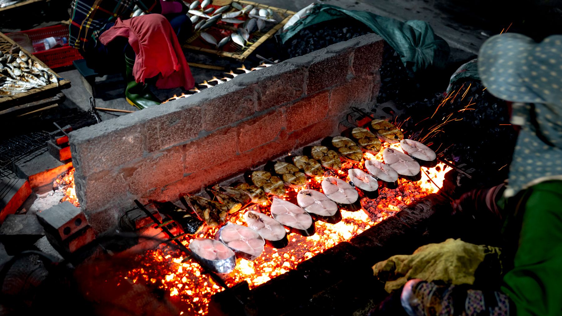 Frischer Fisch wird nachts auf einem belebten Straßenmarkt von lokalen Verkäufern über offenem Feuer gegrillt.