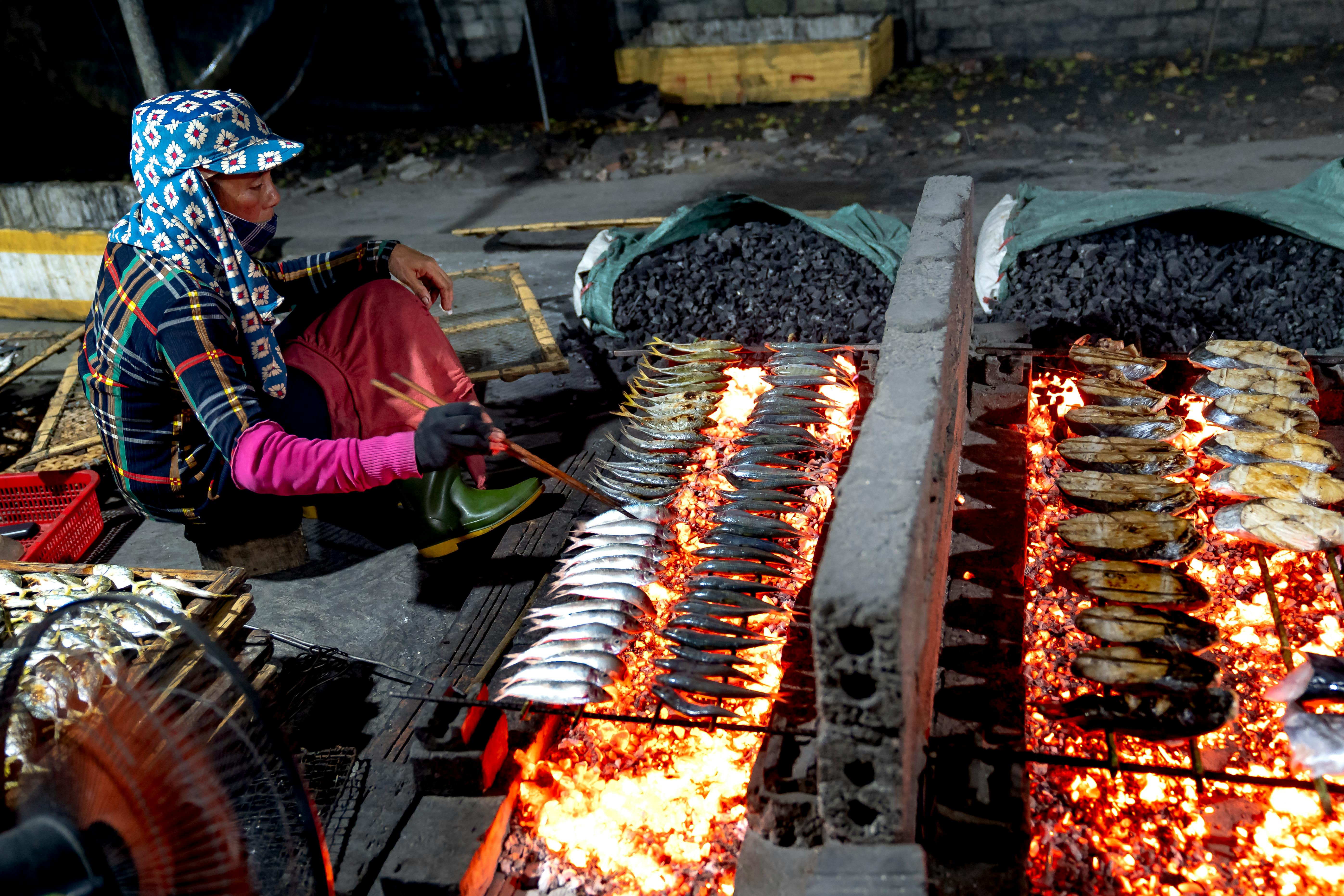 woman grilling fish on a street market