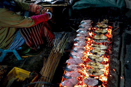 Traditional street vendor grilling a variety of fish over charcoal at night.