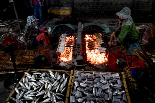 Vendors grilling fish over open flames in an outdoor market setting at night.