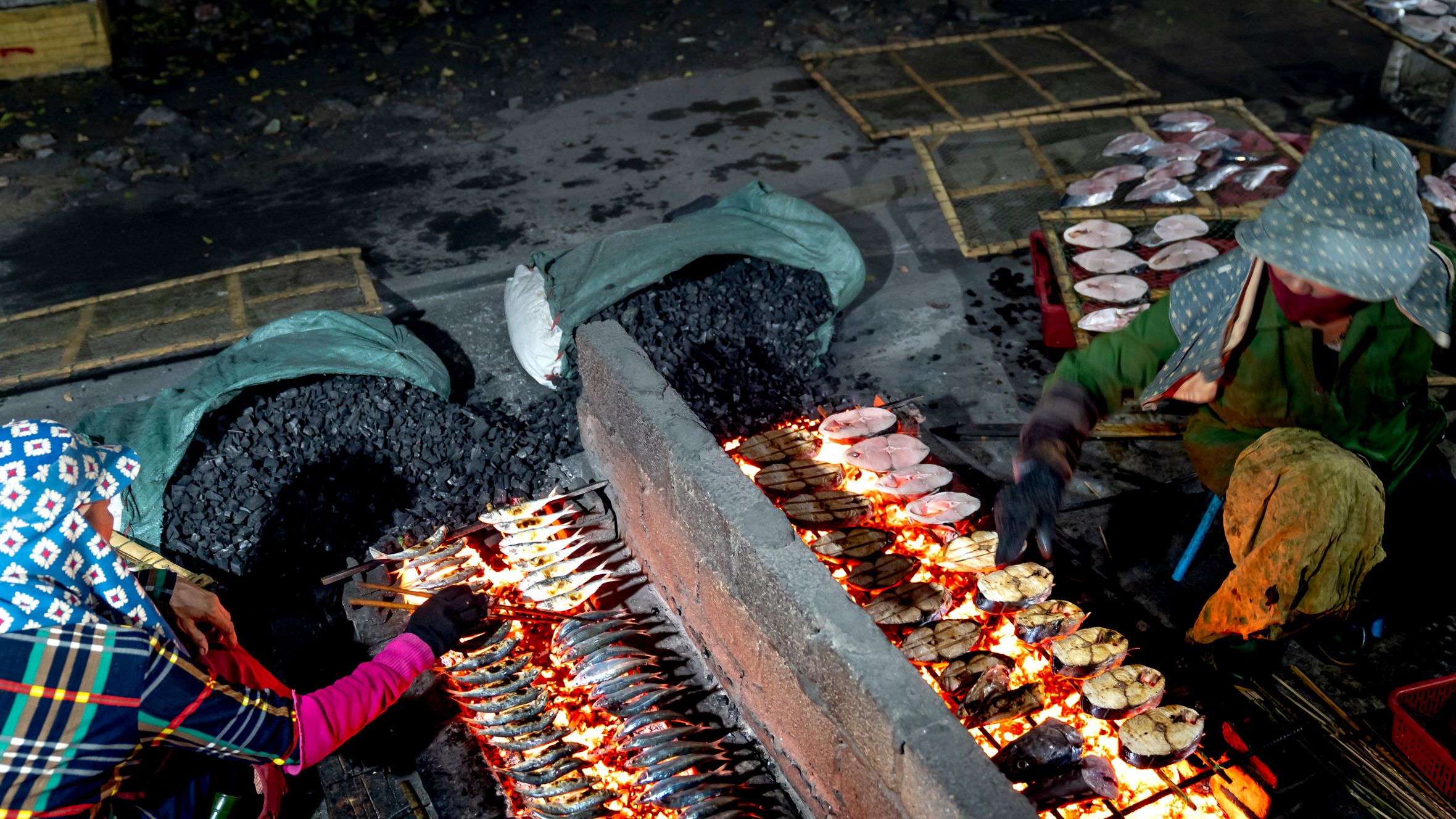 Vendors grilling fish over an open flame at an outdoor street market.