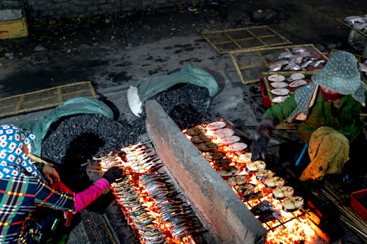 Vendors grilling fish over an open flame at an outdoor street market.