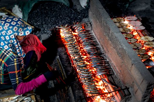 Person grilling fish over open coals, creating smoky and aromatic seafood.