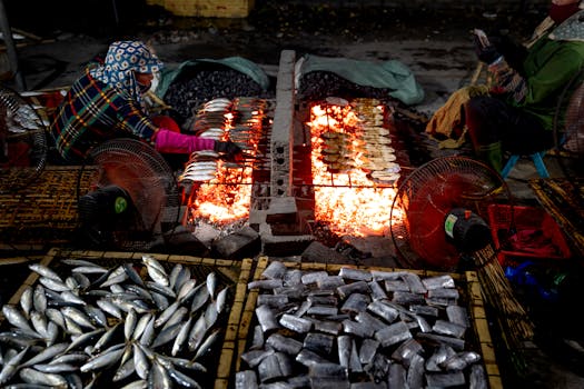 A vibrant scene of fish being grilled over an open flame in a bustling market setting.