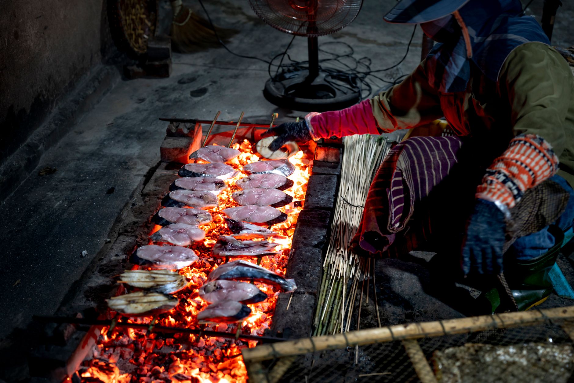 Person roasting fresh fish on an open fire grill in an indoor setting.