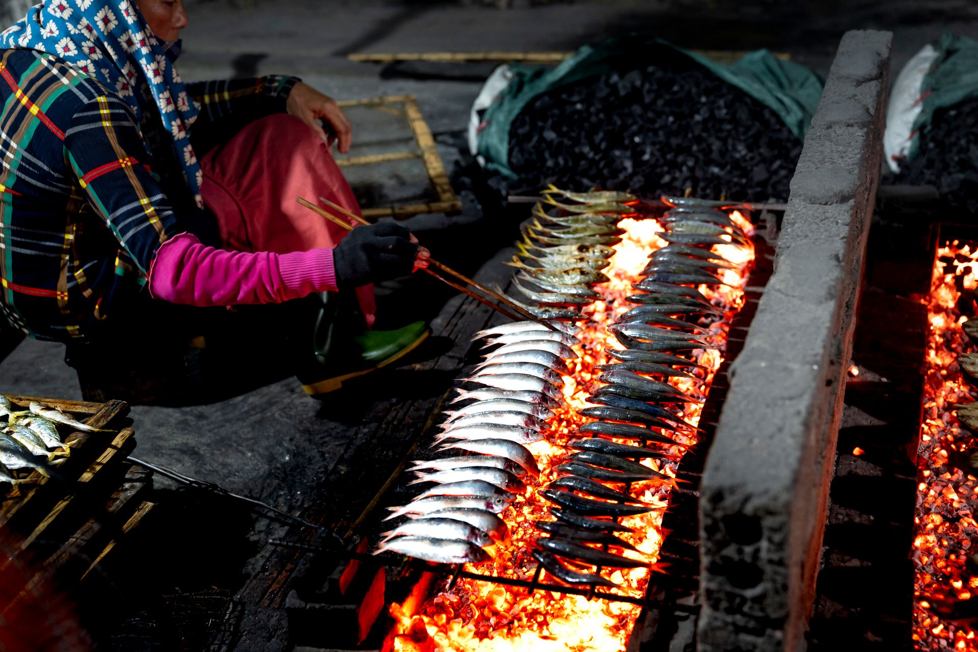 Person grilling fish over open fire at night, showcasing traditional cooking methods.