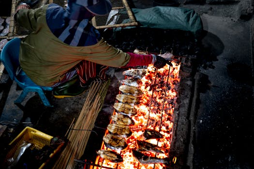A street vendor grills fresh fish on a charcoal fire, capturing traditional cuisine's essence.