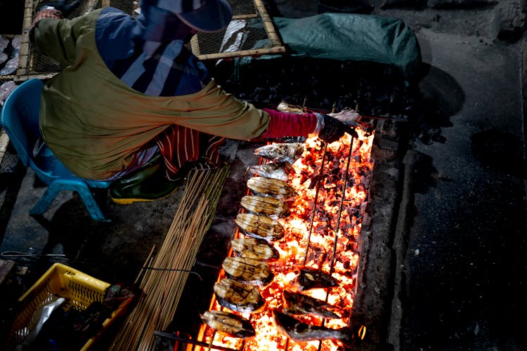 Woman Grilling Fish In A Traditional Way On A Street Market 