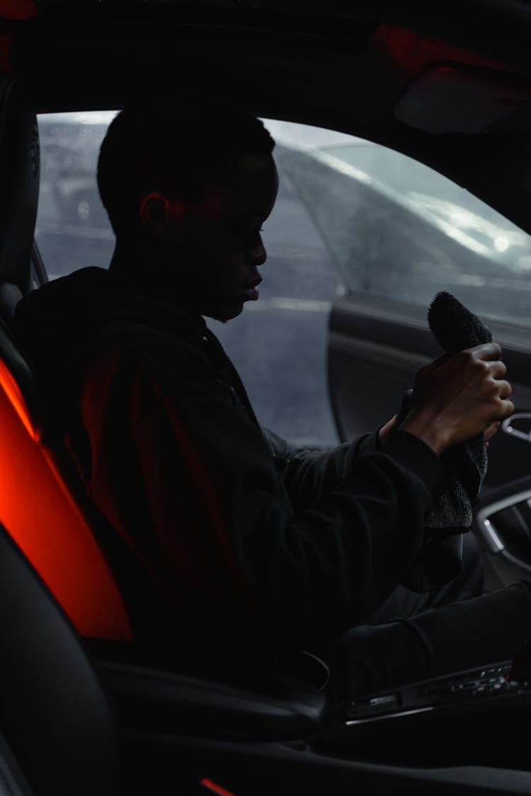 A Man In A Black Hoodie Holding A Towel While Sitting In A Car