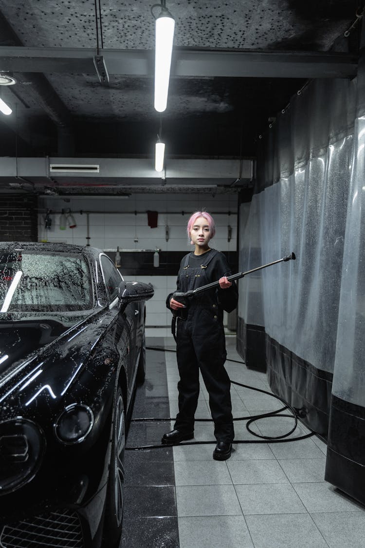 A Woman Standing Beside The Black Car And Holding A Power Spray