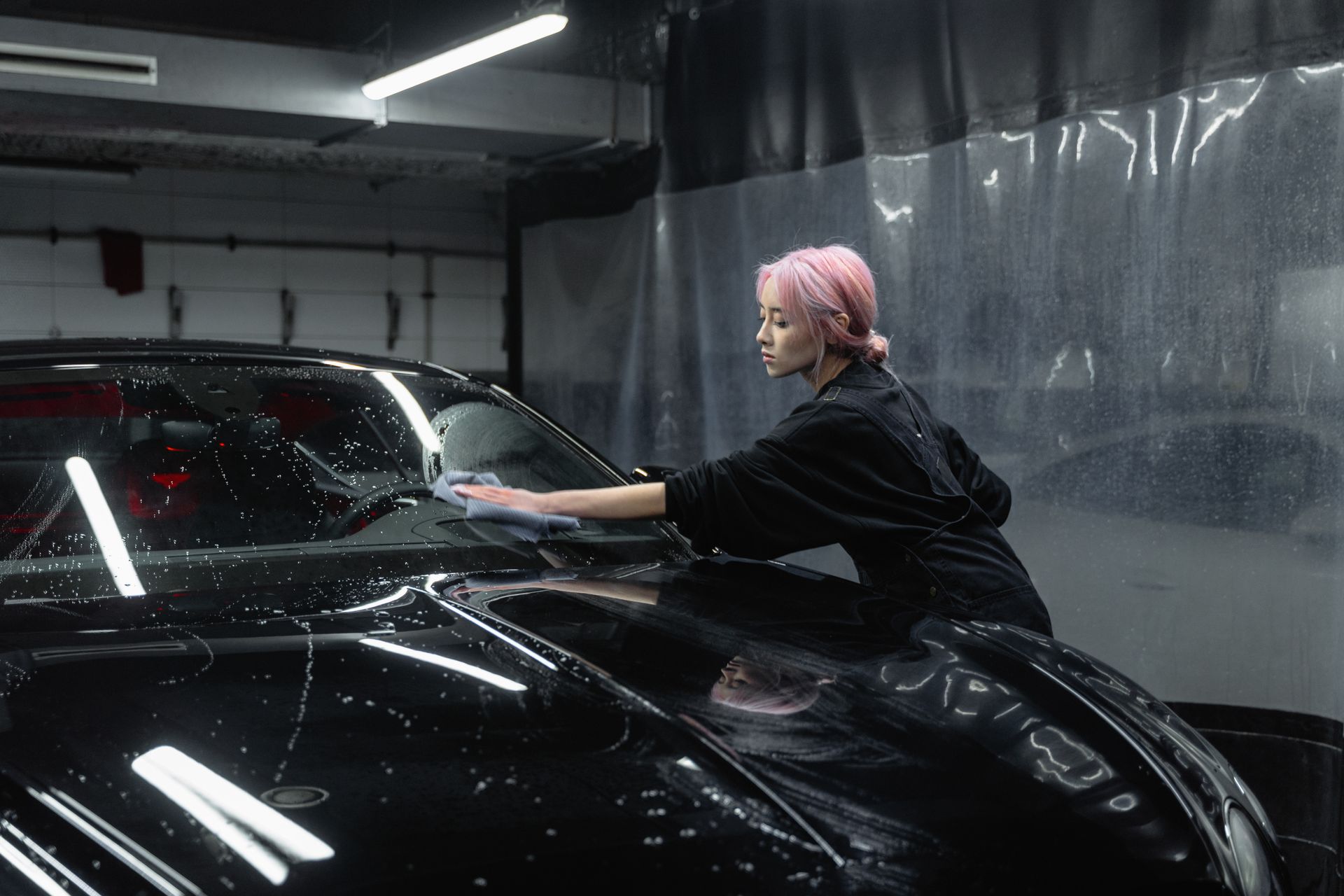 Specialist hand-washing a luxury car inside a foam-filled detailing bay