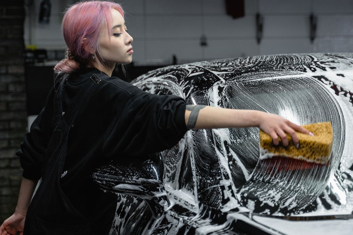 Detailer washing a black car with a soapy sponge