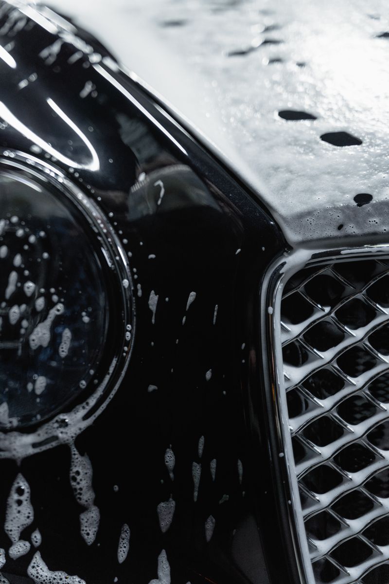 Detailed view of a luxury black car covered with soap suds during a wash.