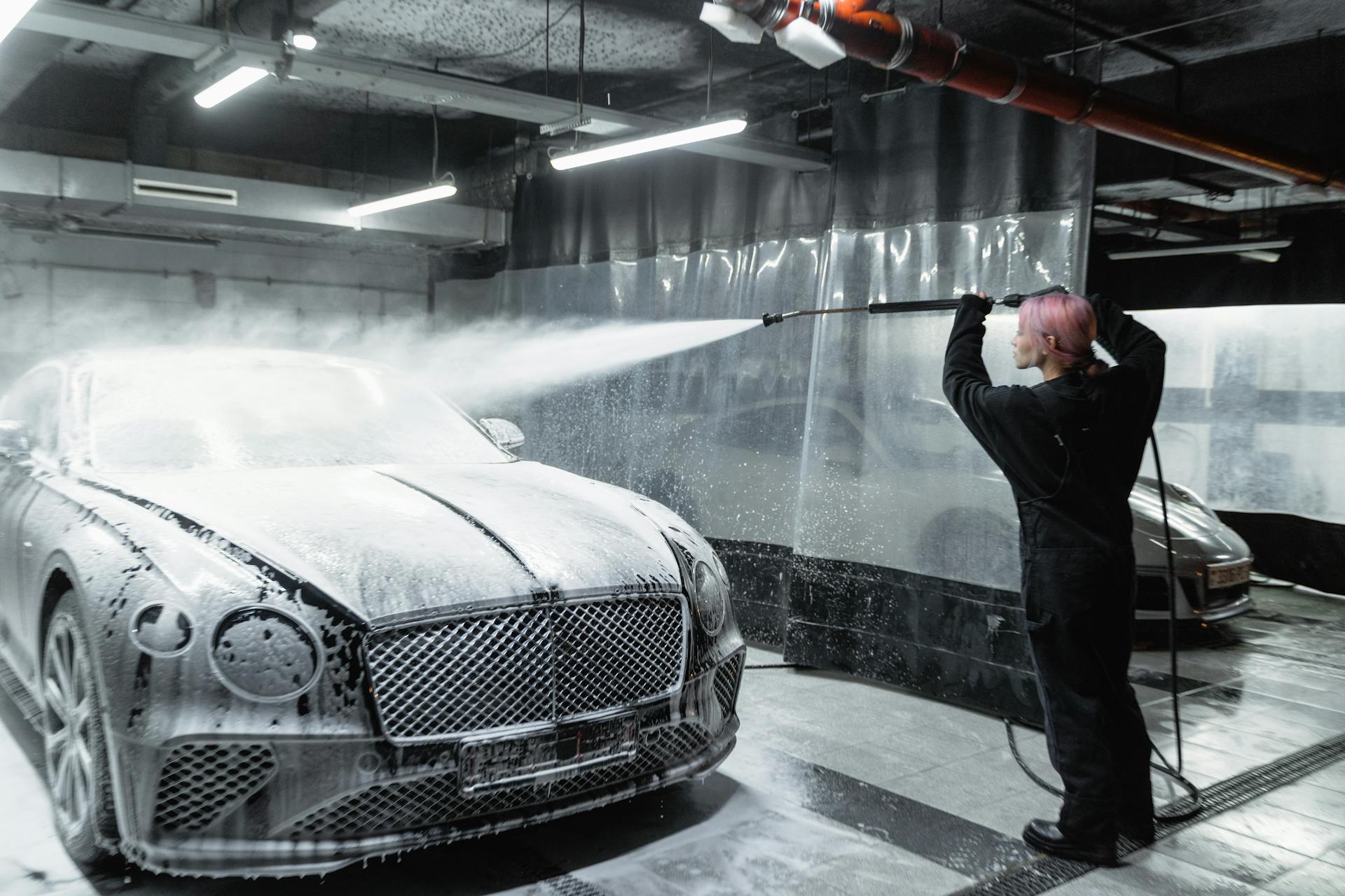 A Woman in Black Jumpsuit Spraying a Snow Foam on a Car