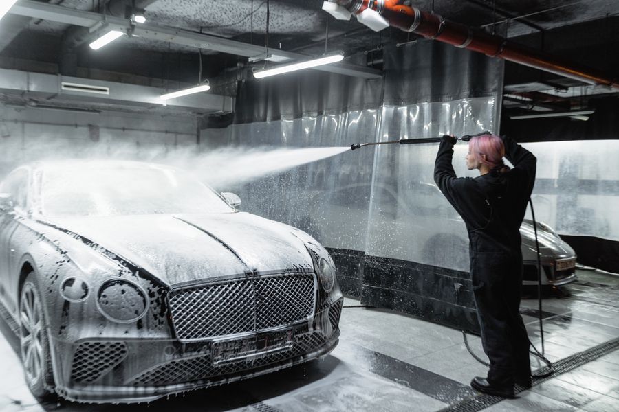 Detailer rinsing a foam-covered car with a pressure wand
