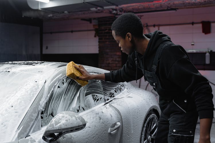 A Man Cleaning A Car Using A Sponge