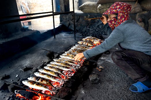 A street vendor grills fish on an open flame, showcasing traditional seafood preparation.