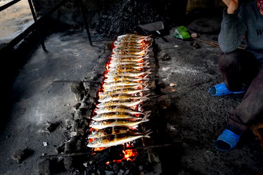 Delicious traditional method of grilling fish over charcoal in an outdoor setting with vibrant flames.
