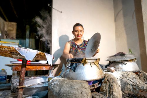 Free Asian woman cooking in traditional outdoor kitchen with steaming pots. Rustic and cultural scene. Stock Photo
