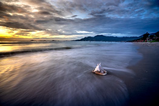 Long exposure of a serene beach during sunset with moody skies and gentle waves.