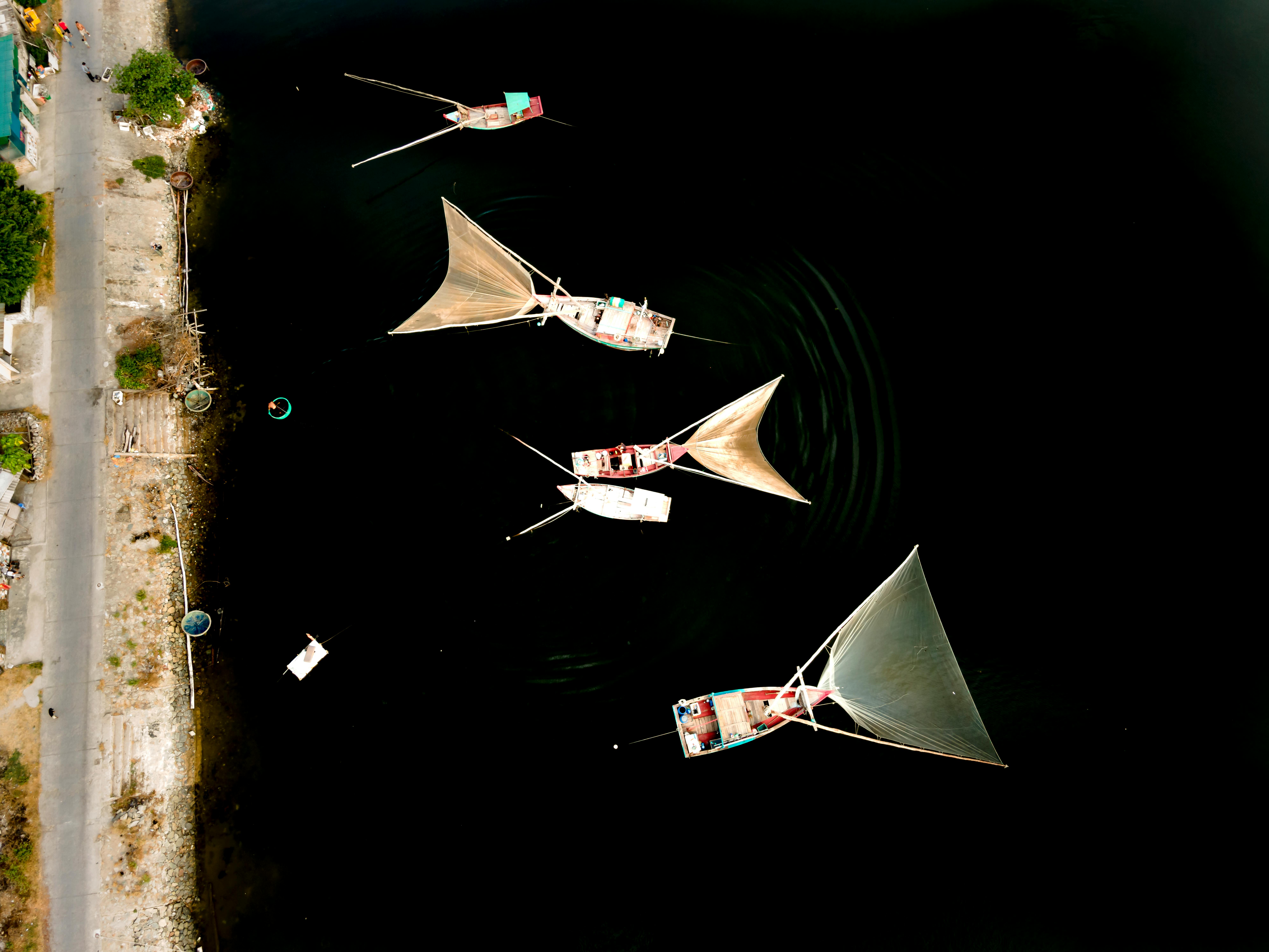 Overhead shot of traditional sailing boats with distinct triangular sails on calm, dark water.
