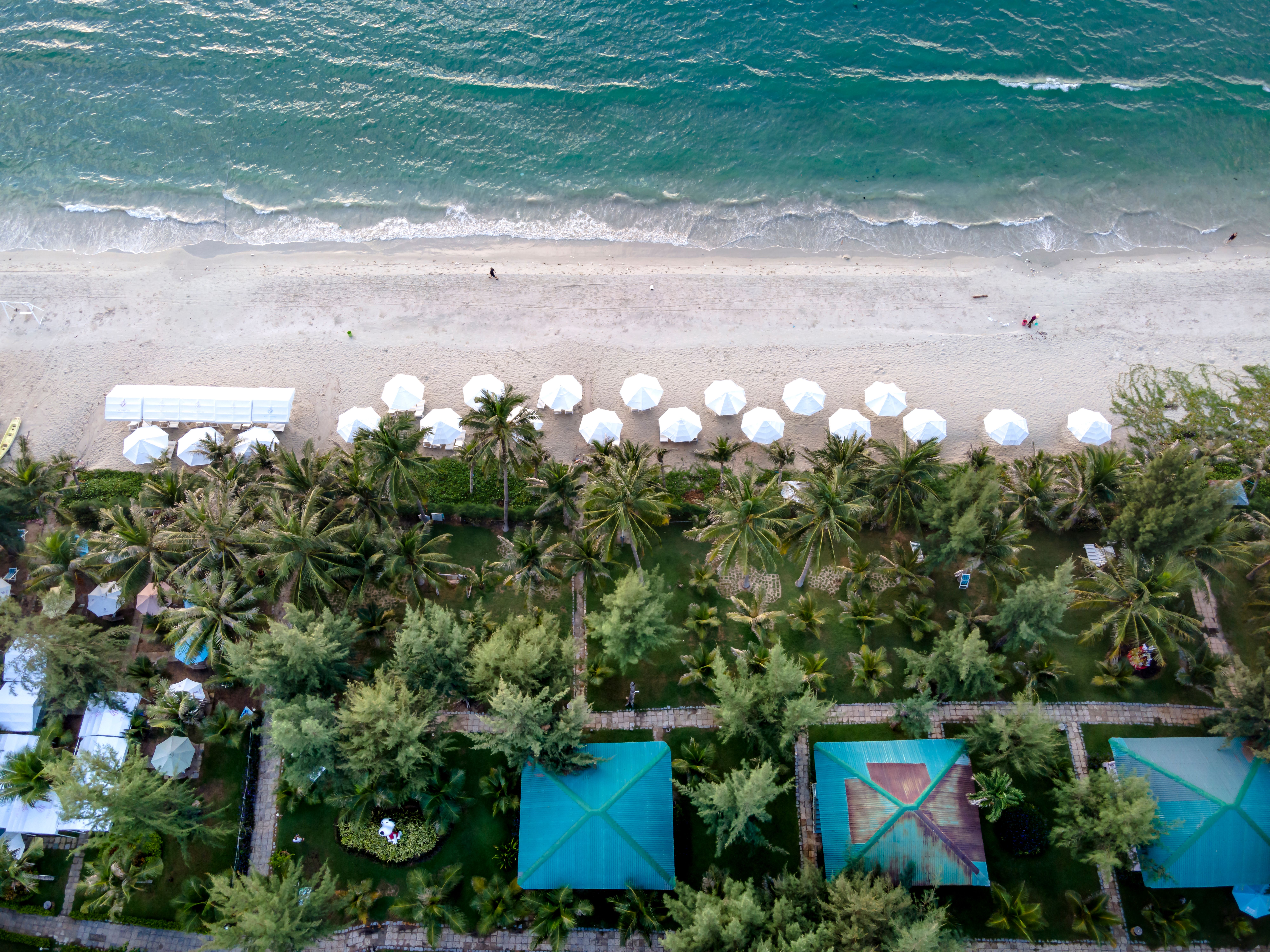 Stunning aerial shot of a tropical beach with white umbrellas and lush greenery.