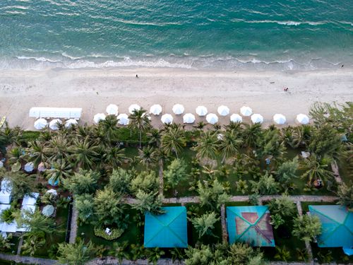 Free Stunning aerial shot of a tropical beach with white umbrellas and lush greenery. Stock Photo