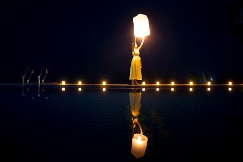 Free Woman in Yellow Dress Holding a Sky Lantern with Light Near the Swimming Pool Stock Photo
