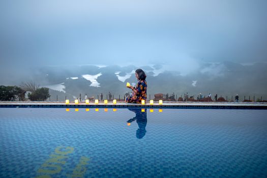 A woman enjoys a tranquil moment beside a foggy pool lit by candles.