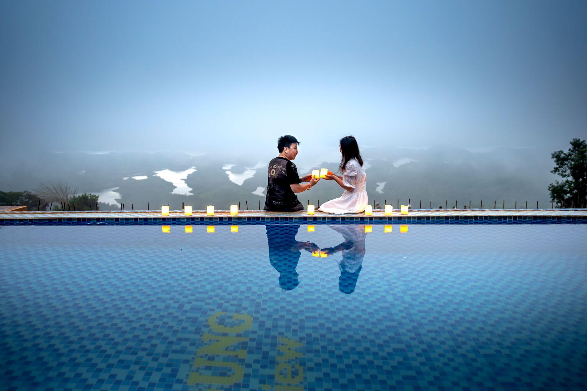 Romantic scene of a couple sharing candles by a serene pool with a misty backdrop.