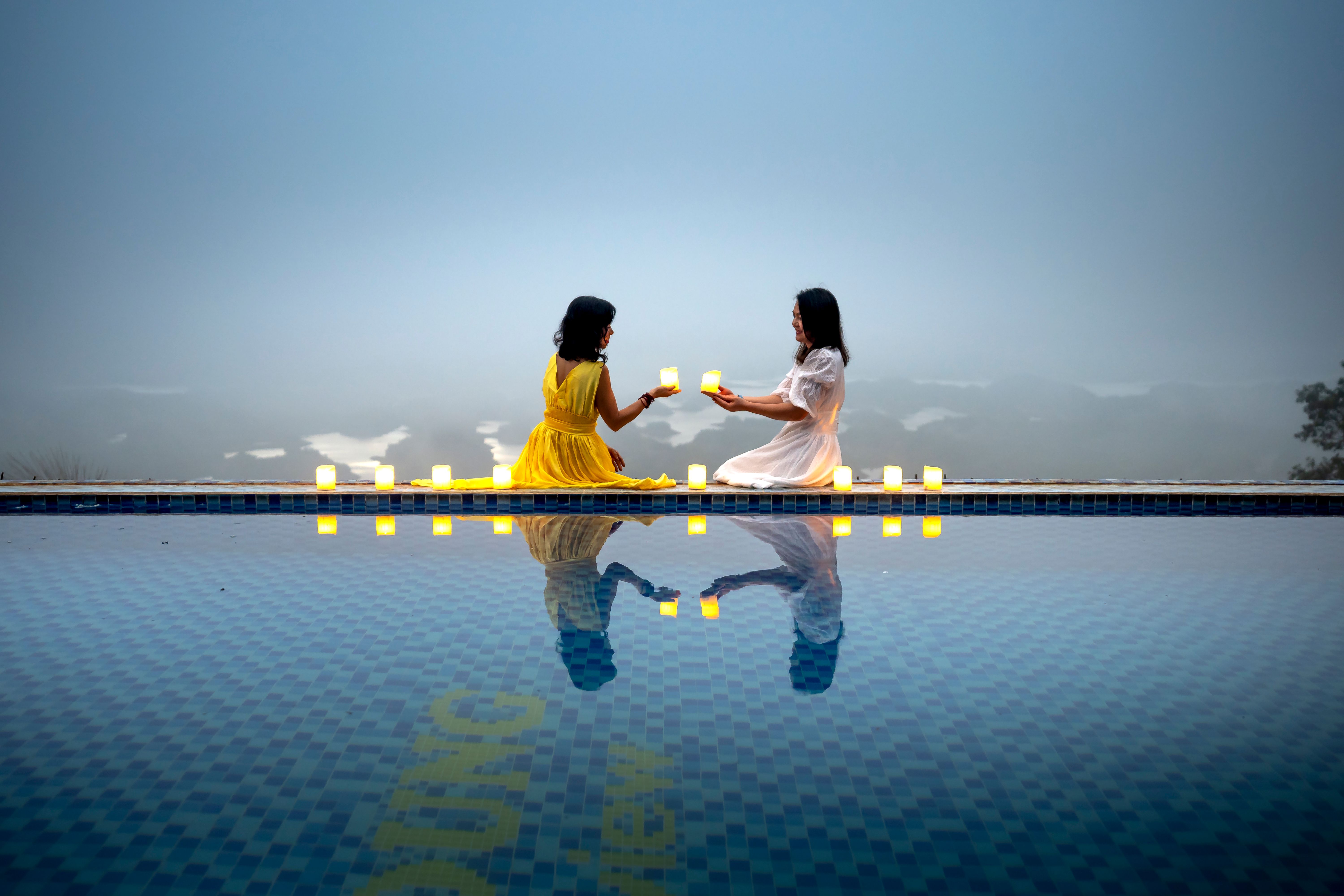 Two women enjoying a peaceful evening by the pool, surrounded by candles.