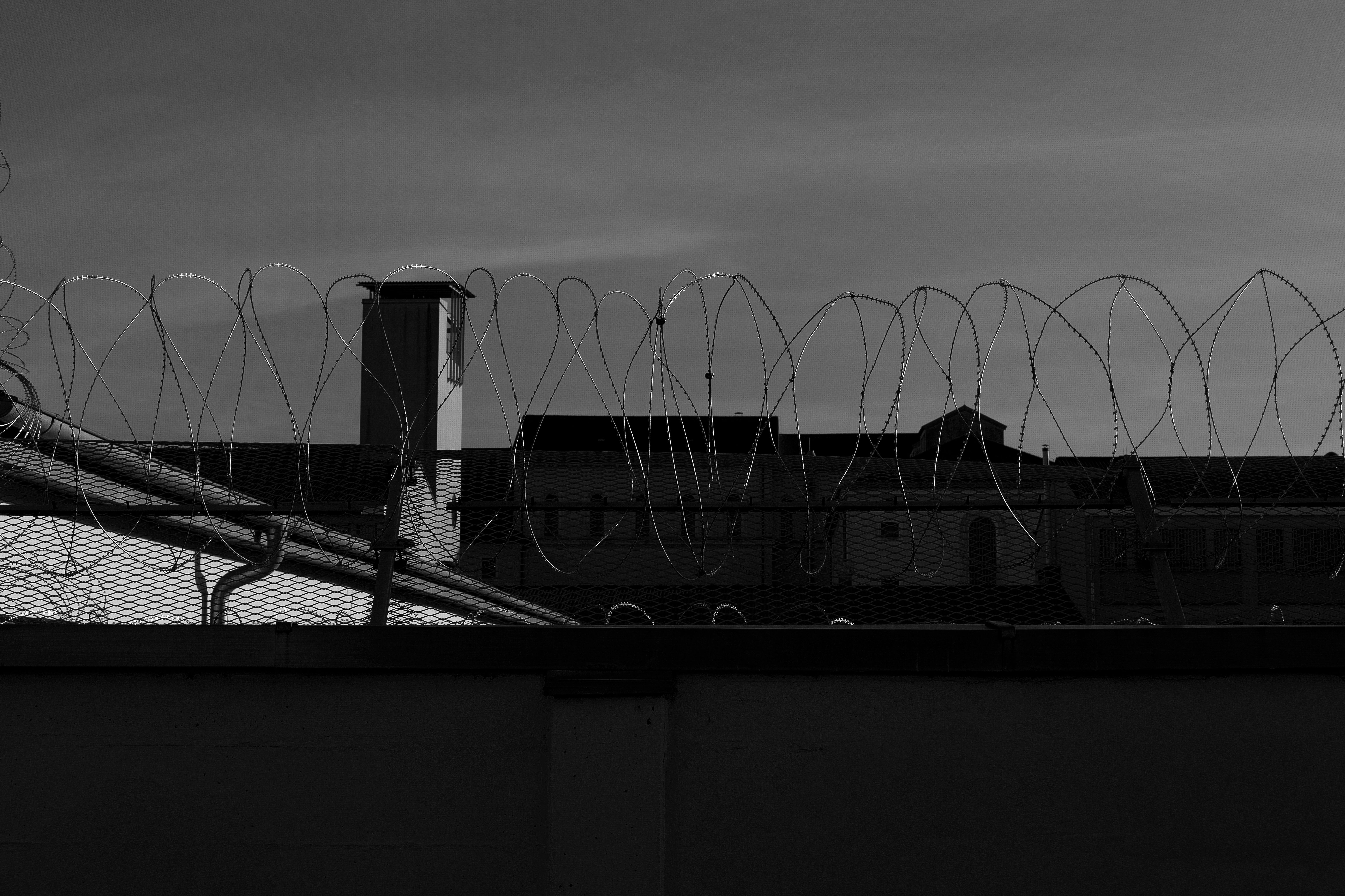 Silhouette of barbed wire fence with buildings in the background under a moody sky.