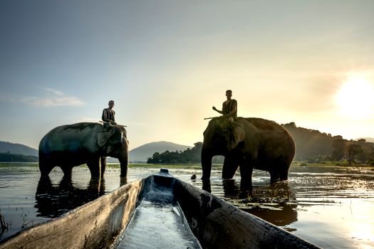 Two elephants with riders in a lake during sunset, picturesque and serene.