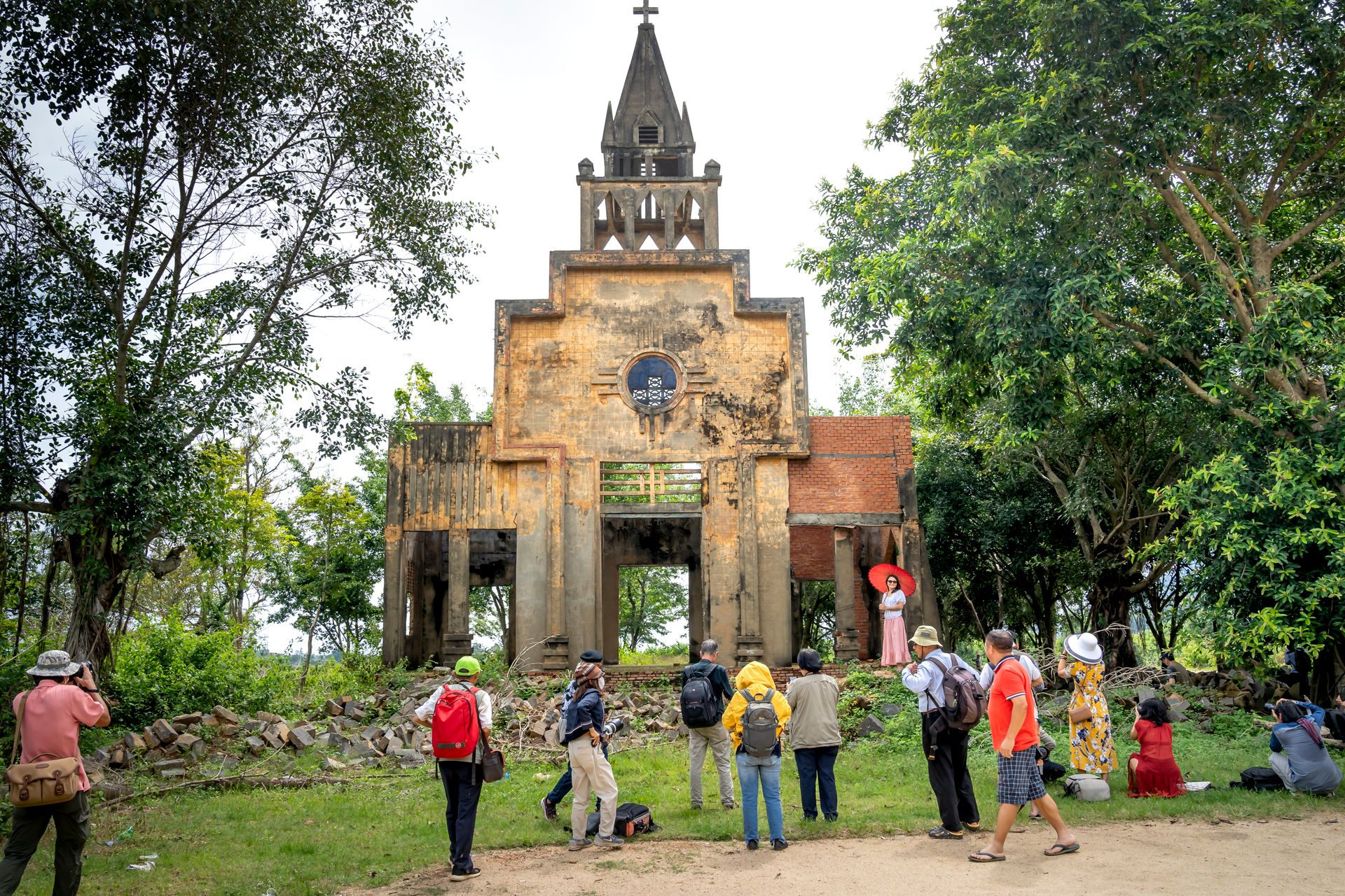 A group of tourists visits a historic, abandoned church ruin surrounded by lush greenery.