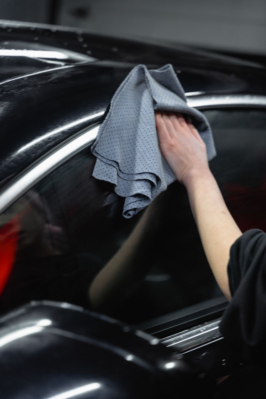 Technician cleaning a black car with microfiber in a dark garage