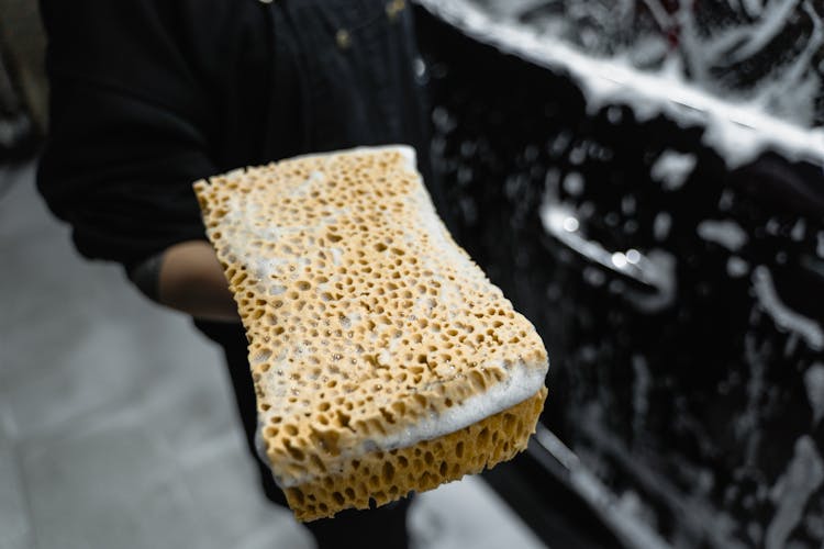 A Person Using A Sponge In Washing Car