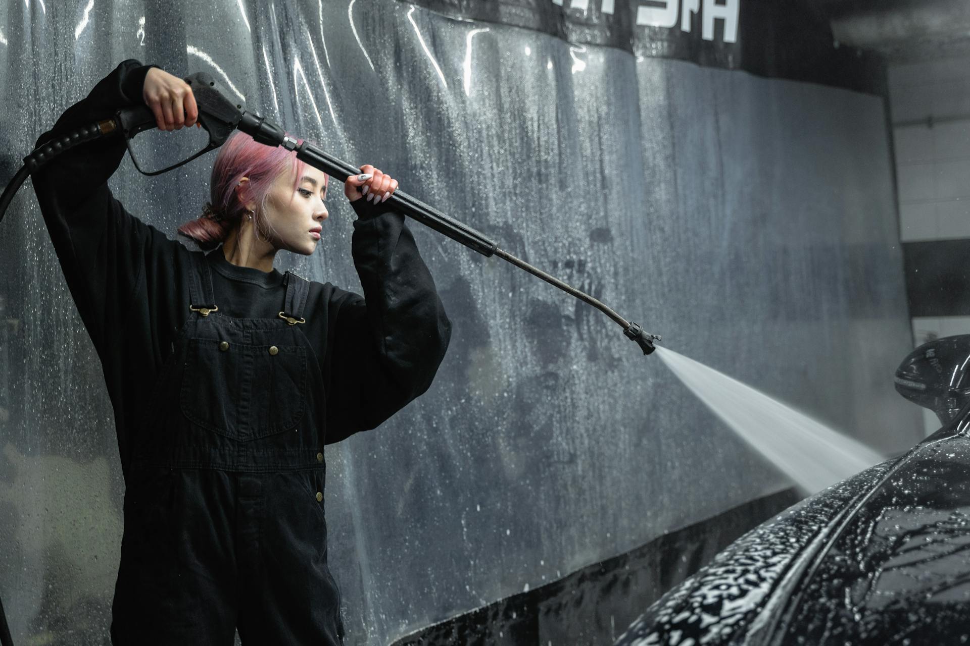 A Woman Washing a Car Using a Pressure Hose