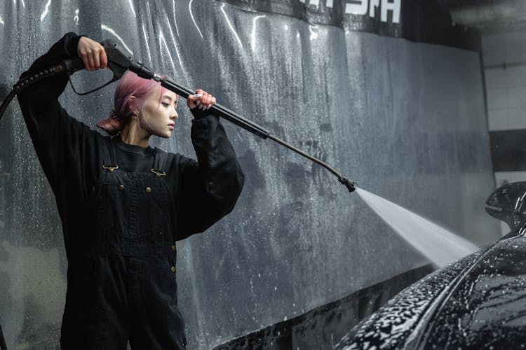 A Woman Washing A Car Using A Pressure Hose