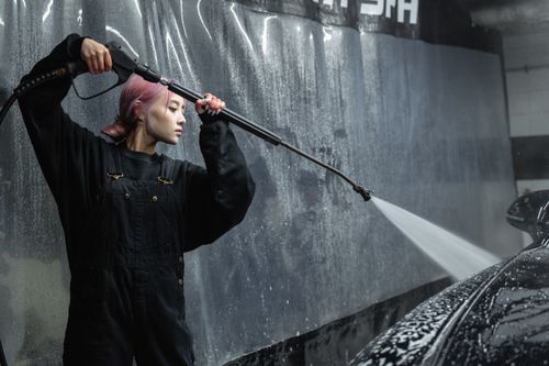 Free A woman using a pressure hose for car cleaning in an indoor garage. Stock Photo