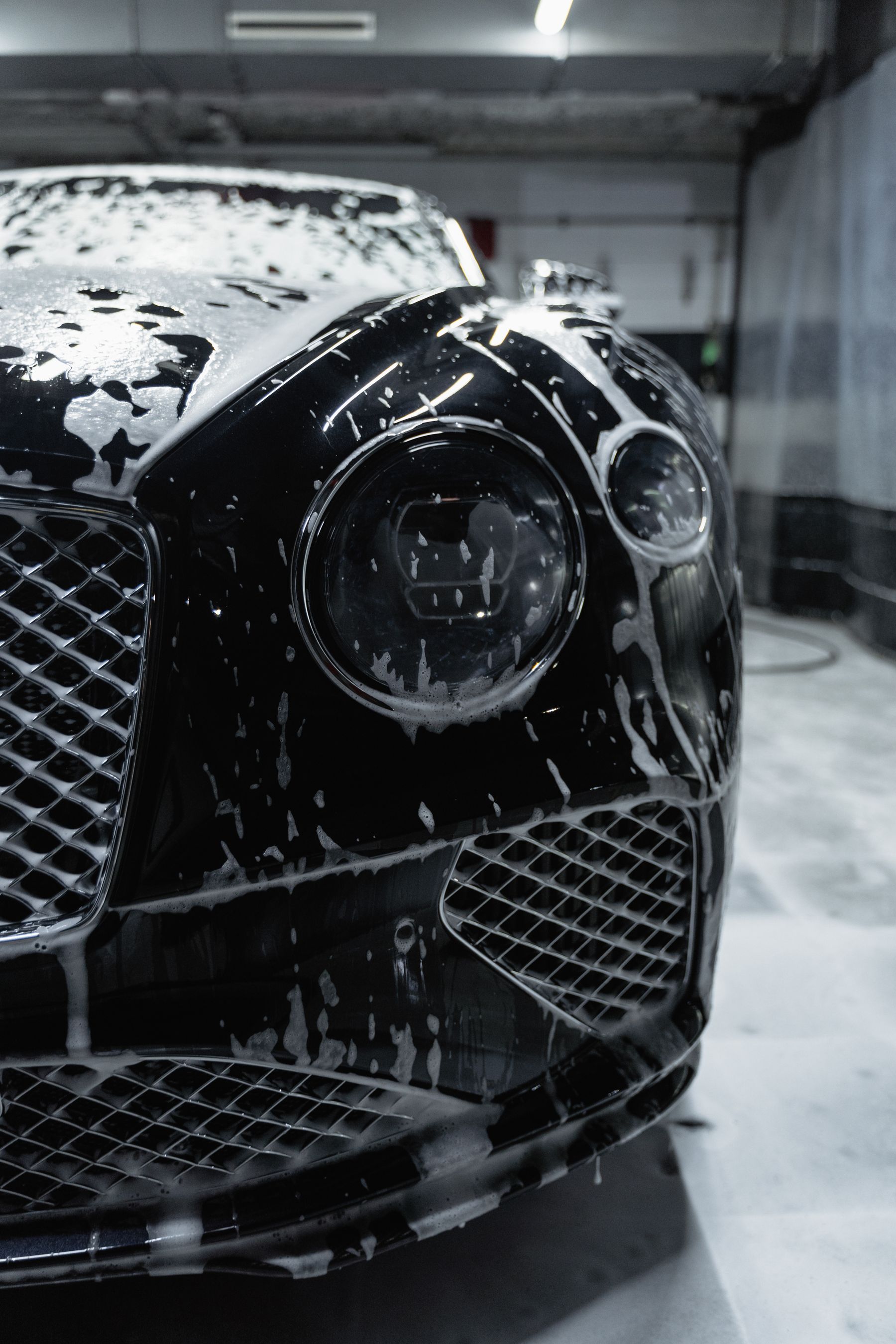 Luxury black sports car covered in foam during a hand wash